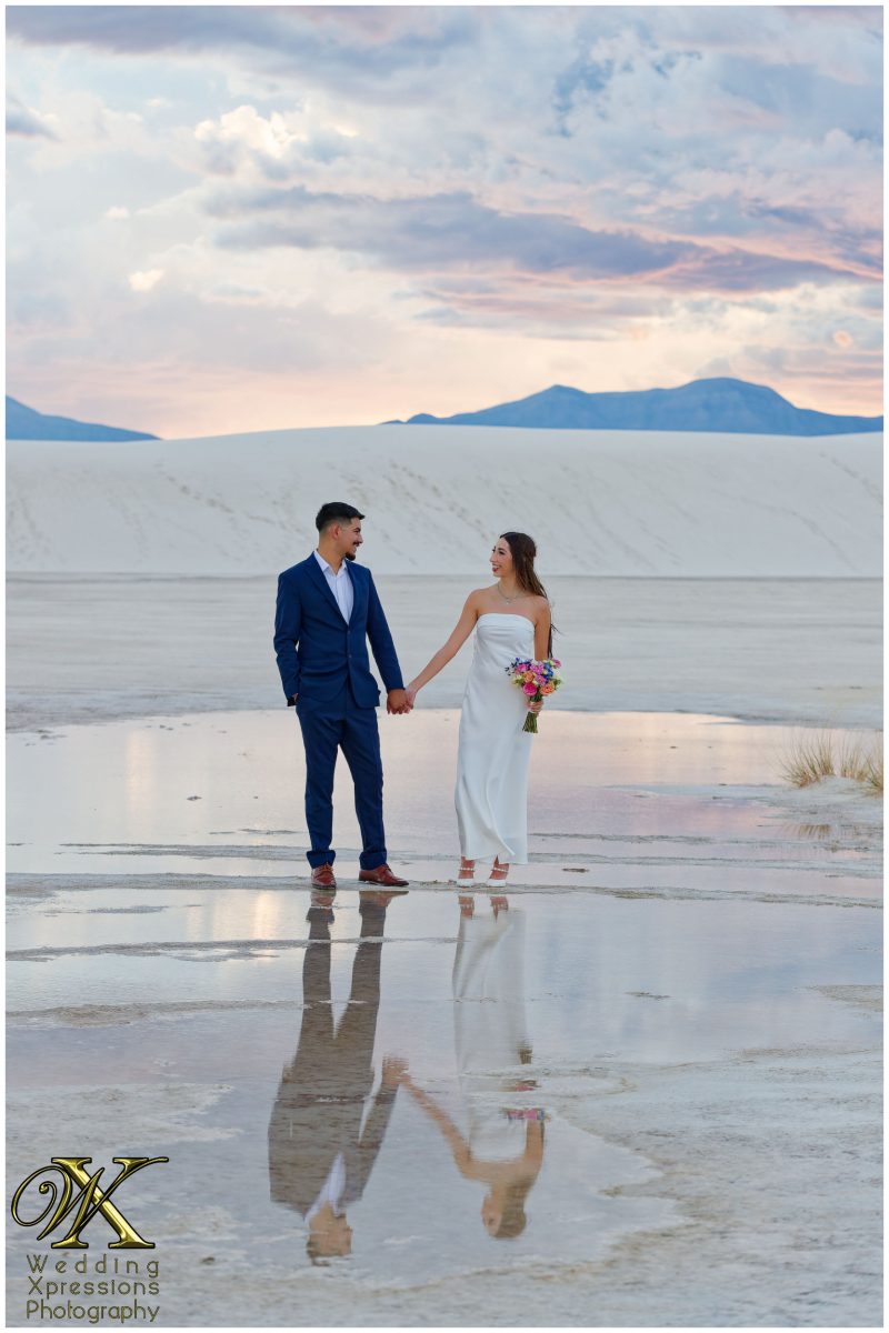 Couple holding hands walking across white desert dunes in New Mexico.