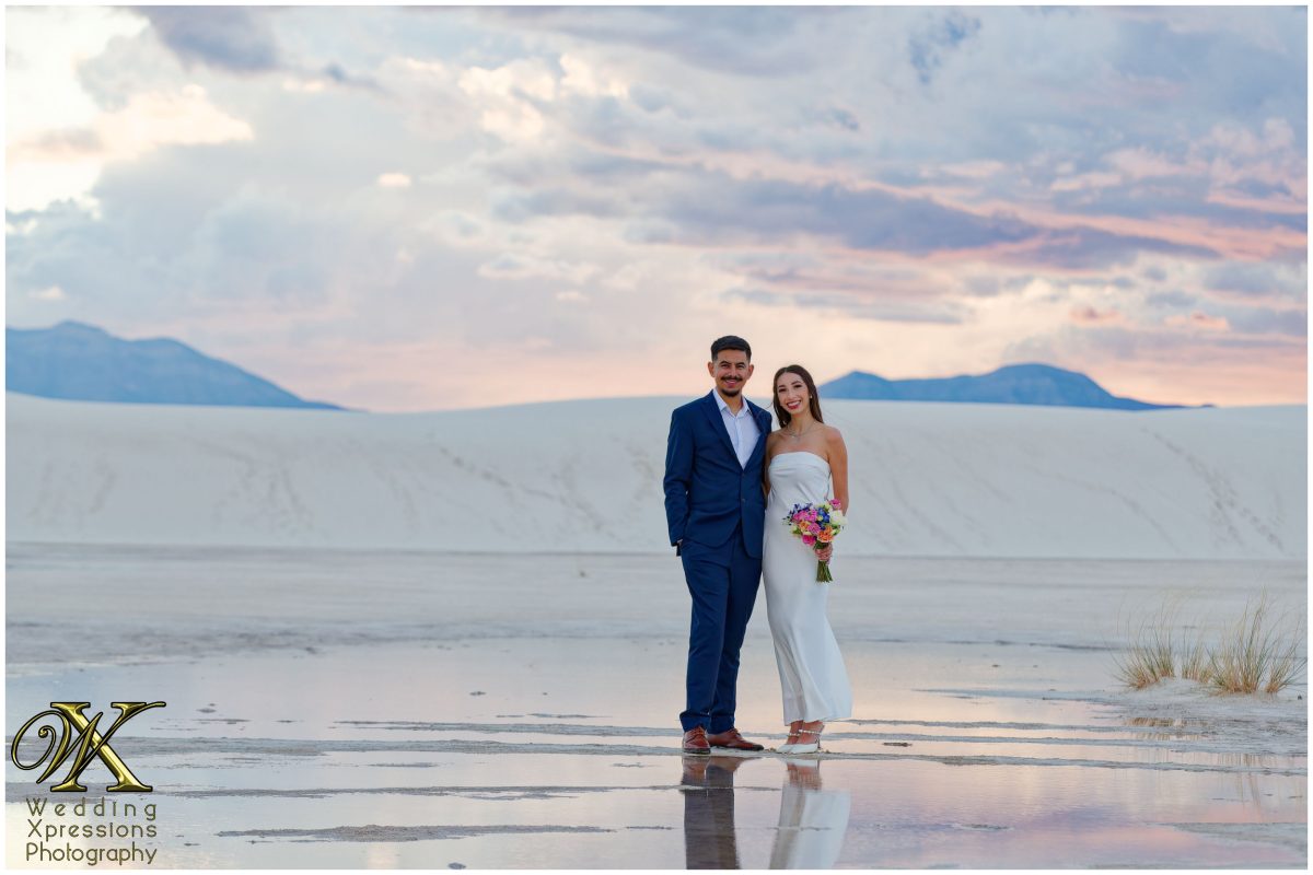Formal portrait of couple on sand dunes with reflection in rainwater.