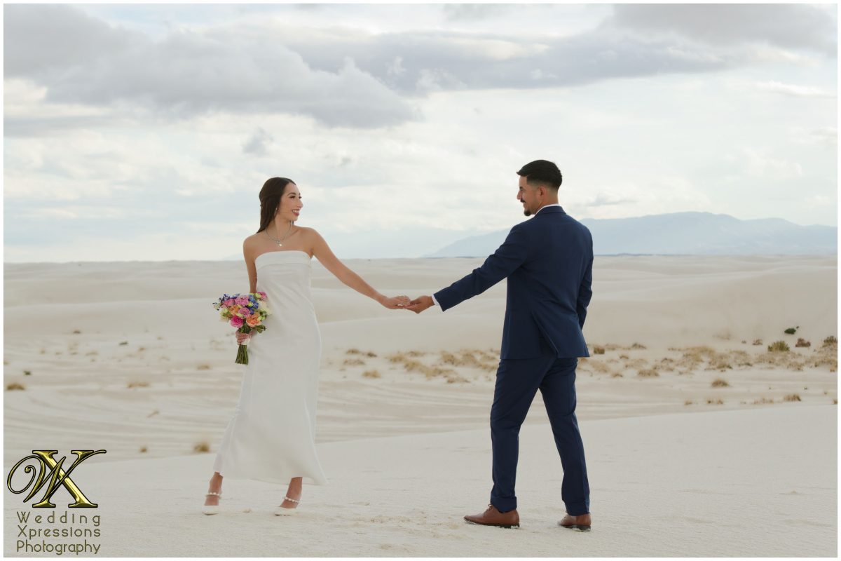 Alan and Illiana holding hands and looking at each other in the dunes.