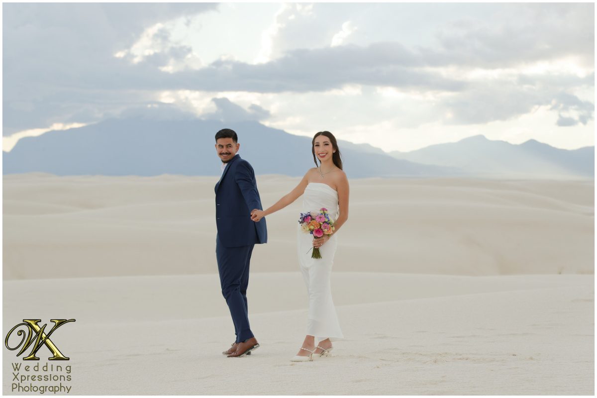 Couple standing apart but holding hands across the sand.