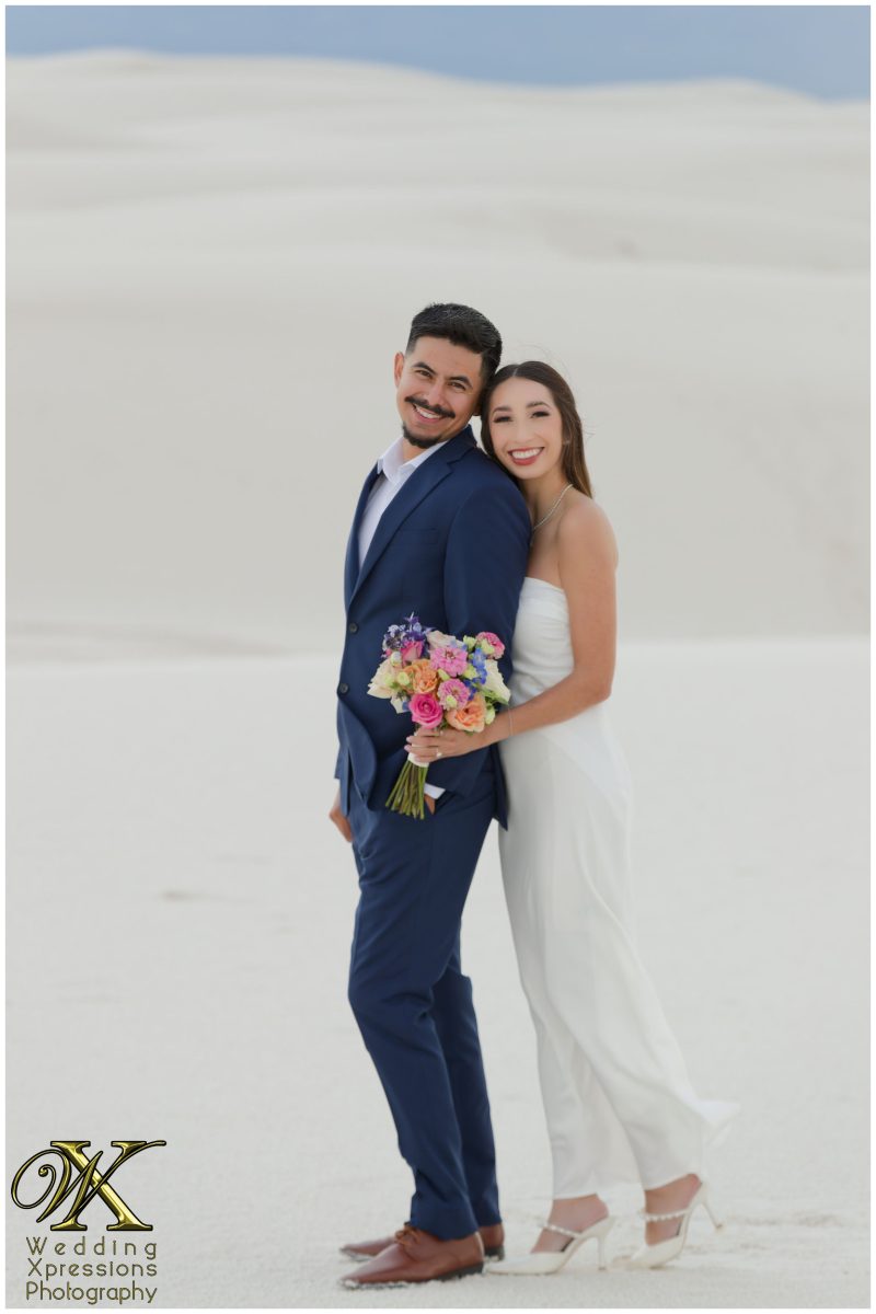 Joyful couple standing together in formal wear in the dunes.