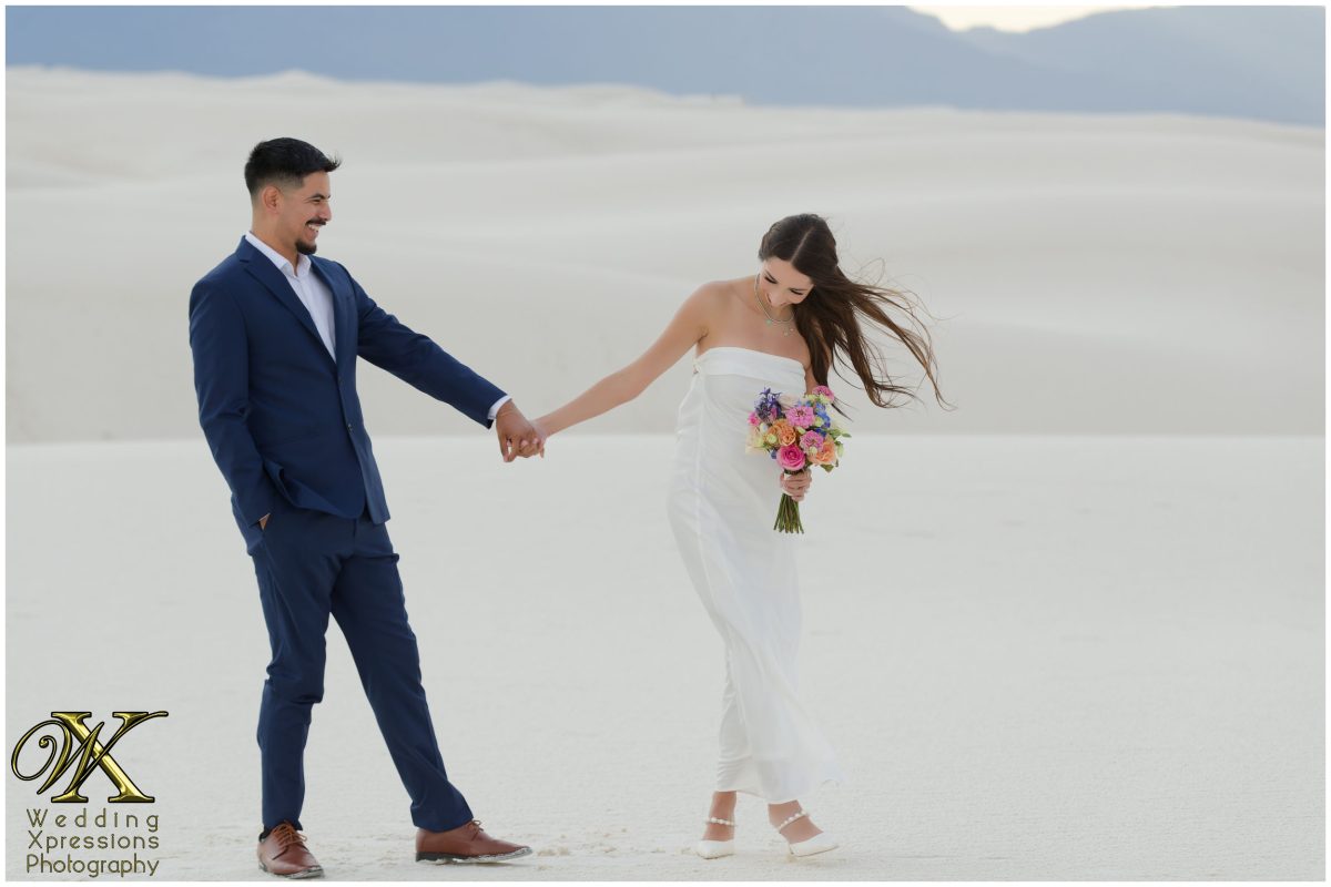 Couple running hand-in-hand toward the camera in the desert.