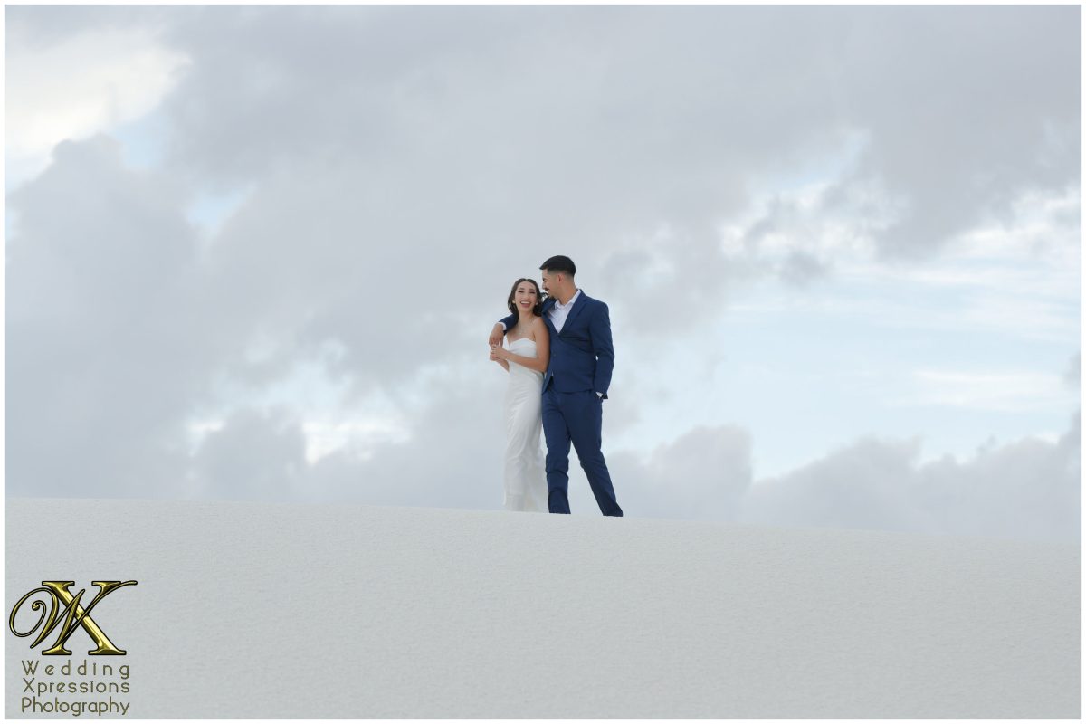 Couple kissing with the white sands stretching behind them.