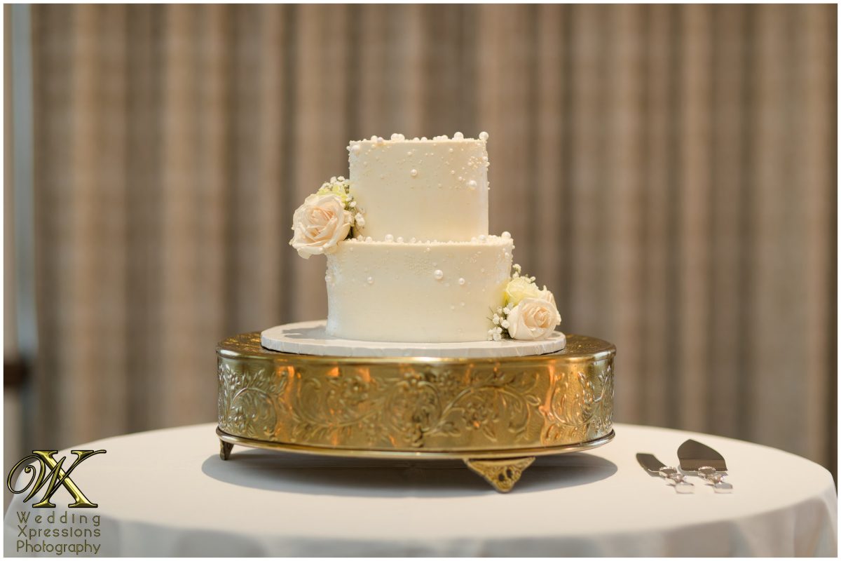Three-tier white wedding cake on a gold stand at The Plaza Hotel reception.